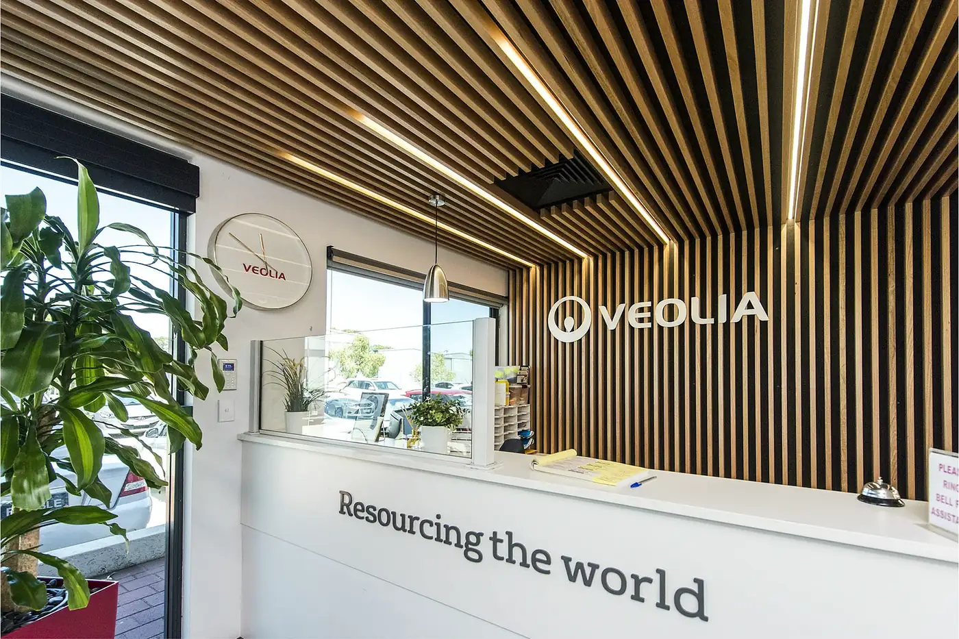 VEOLIA &mdash; reception detail showing the lit timber batten ceiling raking down to the branded wall.